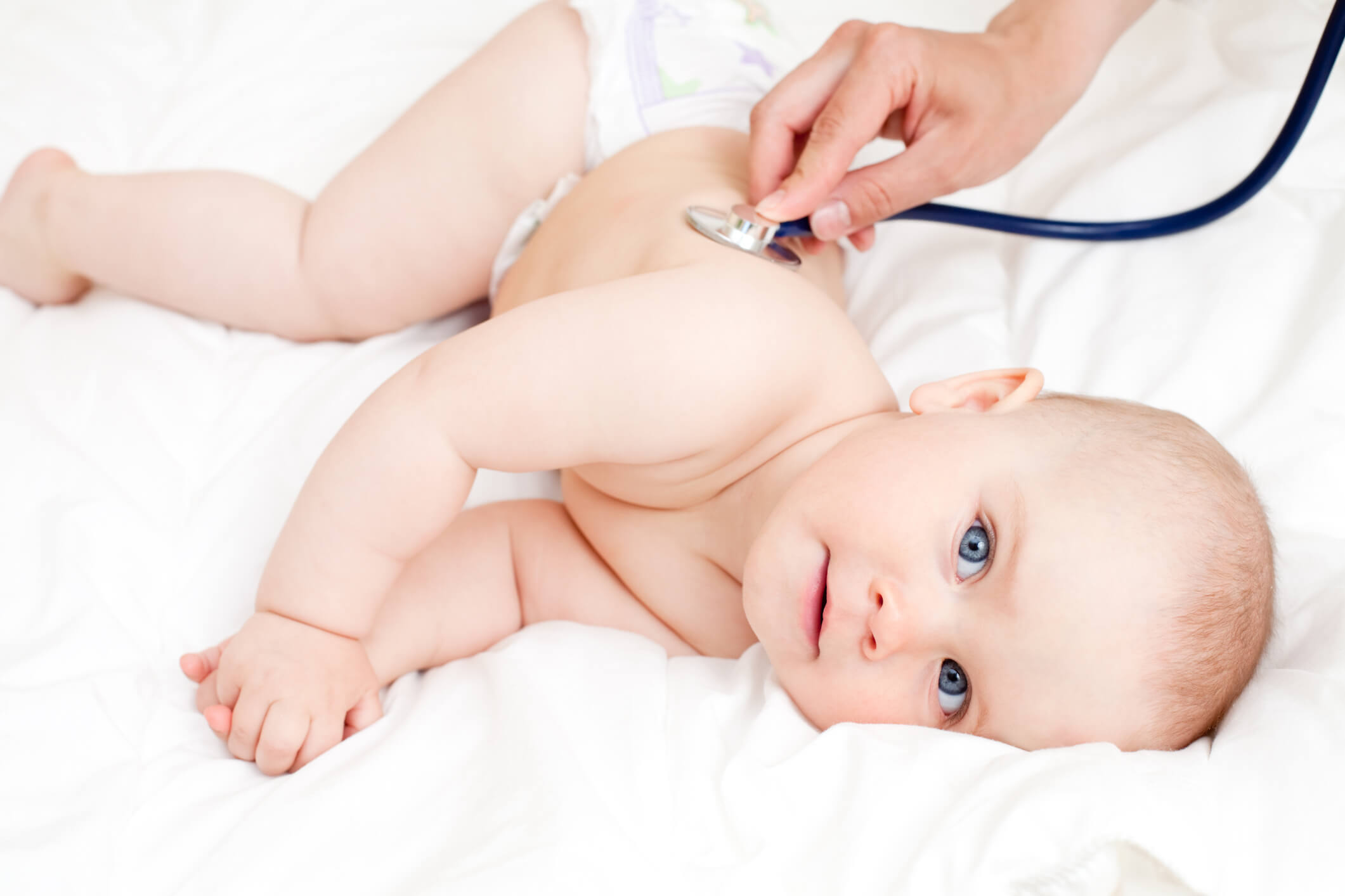 A baby is laying down and a doctors examines the baby with a stethoscope.