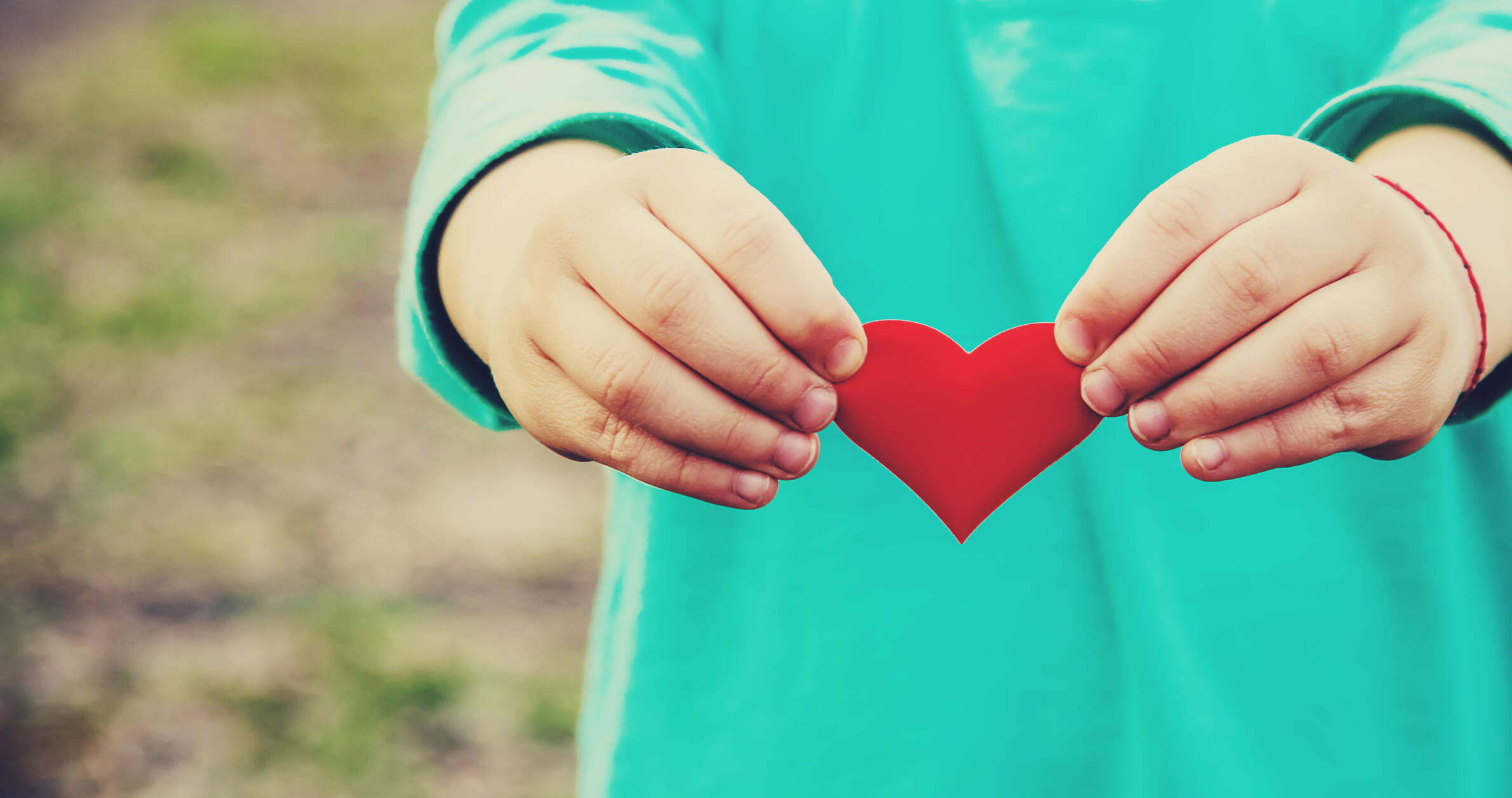 Two hands of a child holding a red heart