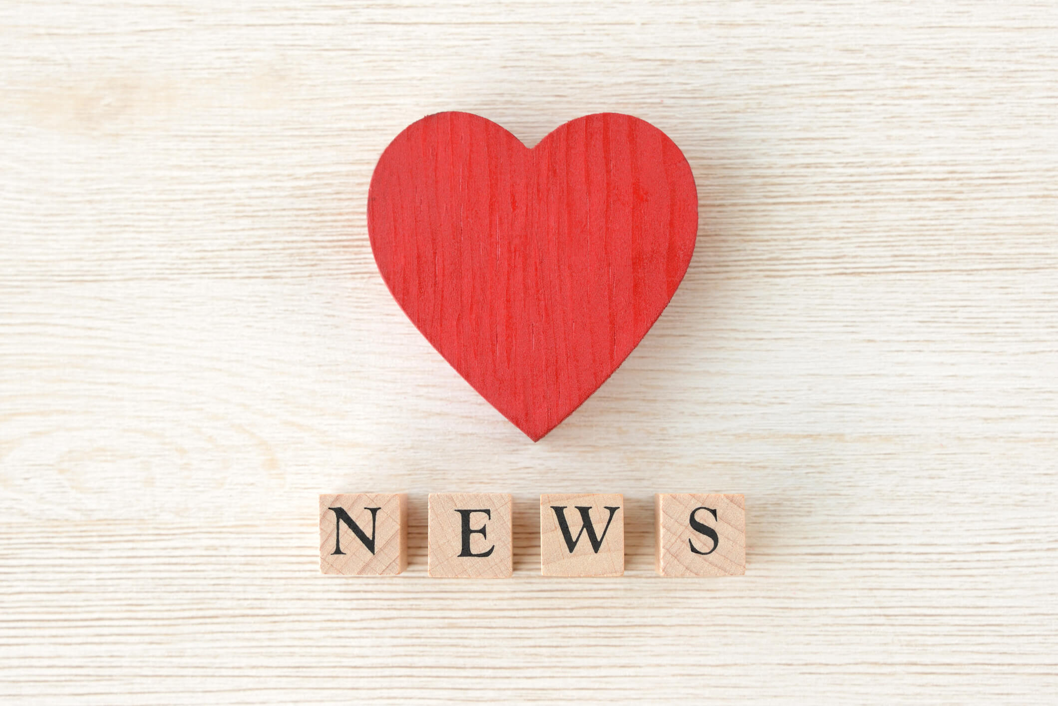 A wooden red heart with wooden letter cubes underneath showing the word news.